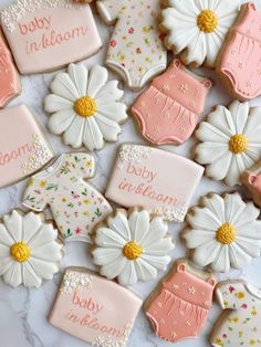 decorated baby shower cookies with pink and white frosting on a marble surface, surrounded by daisies