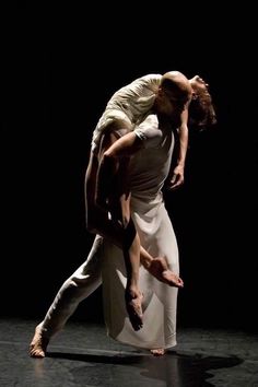 a man and woman dance together in the middle of a dark room with their arms around each other