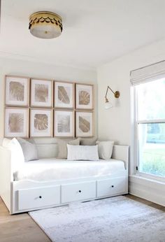 a white daybed with drawers underneath it in front of some pictures on the wall