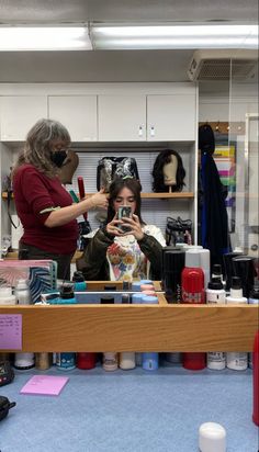 a woman taking a selfie in front of a mirror while another person looks at her cell phone