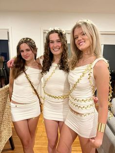 three beautiful women in white dresses posing for the camera with gold chains around their waist