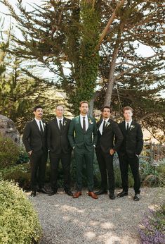 a group of men in suits standing next to each other near trees and bushes on a gravel road