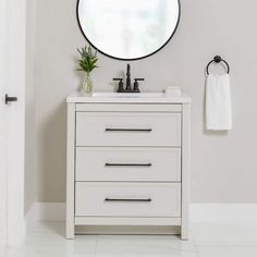 a white bathroom vanity with a round mirror above it and a towel hanging on the wall