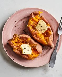 two stuffed sweet potatoes with butter on a pink plate next to a fork and knife