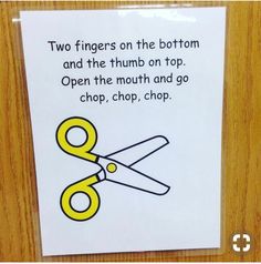 a pair of yellow scissors sitting on top of a piece of paper next to a sign that says two fingers on the bottom and the thumb on top