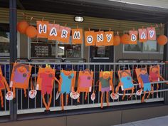 orange and blue paper cutouts are hanging from a metal fence with the words harmony day on it