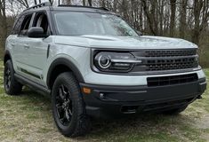 the front end of a white ford bronco parked in a grassy area next to trees