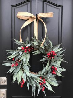 a wreath with red berries and green leaves hanging on the front door