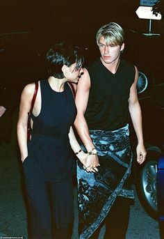 a man and woman holding hands while standing next to each other in front of a car