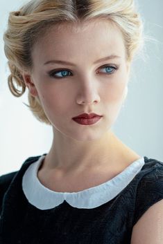 a woman with blonde hair and blue eyes wearing a black dress is looking at the camera