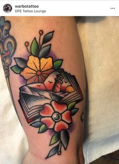 a tattoo on the leg of a woman with an open book and flowers in it