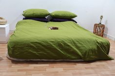 a bed with green sheets and pillows on top of it in a room that has wooden floors