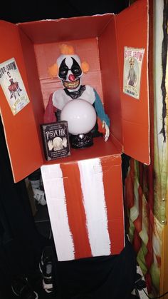 a creepy doll in a box with an orange and white striped wall