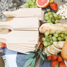 an assortment of cheeses, fruit and bread on a picnic table