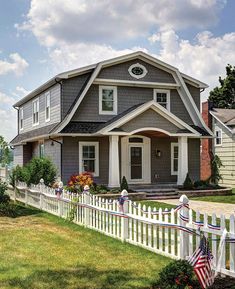 a house with a white picket fence and american flag on the front lawn in front of it