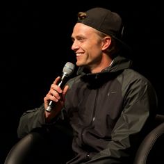 a man sitting in a chair holding a microphone and talking into a microphone with a black background