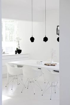 a white table and chairs in a room with black lamps hanging from the ceiling above it