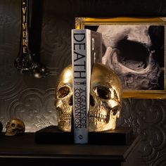 two golden skulls sitting on top of a black table next to a bookend with a skull in front of it