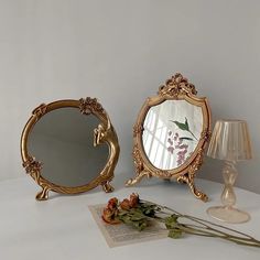 two mirrors sitting on top of a white table next to a lamp and flower vase