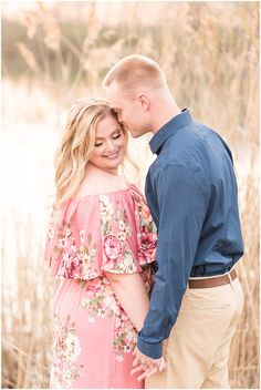 a pregnant couple cuddles close to each other in front of tall grass