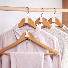 clothes hanging on wooden hangers in front of a white wall