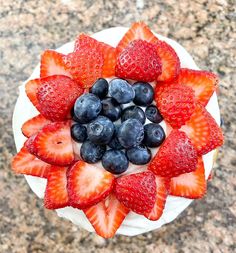 a cake topped with strawberries and blueberries on top of a marble countertop