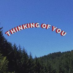 a sign that says thinking of you in front of some trees and blue sky behind it