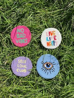 four badges with words on them sitting in the grass, one has an eye and two says we live map