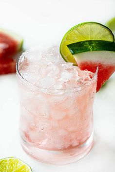 a watermelon and cucumber cocktail garnished with limes on a white surface