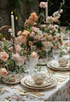 the table is set with pink roses and china dishes, candles, and flowers in vases