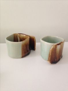 two small cups sitting on top of a white table next to each other, one with brown and blue glaze