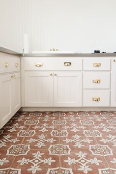 a kitchen with white cabinets and red tile flooring in the center, along with an ornate pattern on the floor