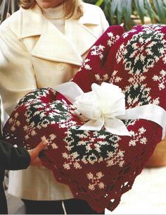 a woman holding a heart shaped pillow with a white flower on it and wearing a coat