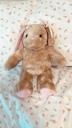 a brown stuffed animal sitting on top of a bed covered in pink and white sheets