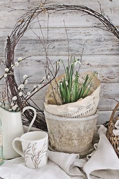 an old bucket filled with flowers next to two coffee mugs and a wicker basket