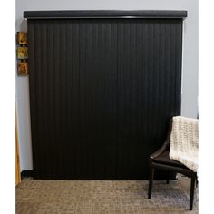 a chair sitting in front of a black paneled wall with vertical blinds on it