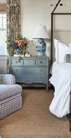 a bed room with a neatly made bed next to a chair and a dresser in front of a window