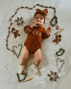 a baby laying on the floor with christmas decorations around it and chewing on a spoon