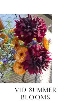 a vase filled with colorful flowers on top of a table next to the words mid summer blooms