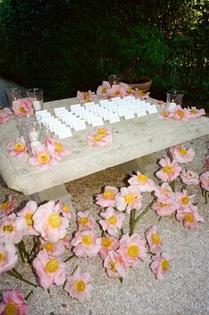 a wooden table topped with lots of pink flowers next to glasses and candles on top of it