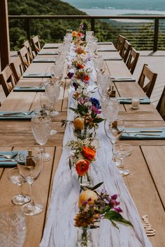 the long table is set with flowers and wine glasses for an outdoor dinner party overlooking the ocean