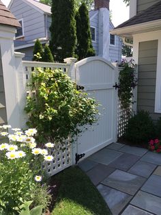 a white picket fence in front of a house with flowers growing on the side walk