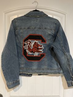 "Custom painted University of South Carolina Jacket.  *These are made to order. I currently do not have any completed of this design in stock. Please include the following information when purchasing: 1. Design idea (if different from photo) 2. Size of jacket  3. Date needed by (please note I have a 3-4 week processing time at the moment. if you need the jacket sooner please reach out to confirm with me that I can have it processed by the date you need it before purchasing) 4. Optional: any othe Team Logo Design, Custom Denim Jacket, Hand Painted Denim Jacket, Painted Denim Jacket, University Of South Carolina, Custom Denim, Painted Jeans, Painted Denim, Painted Clothes