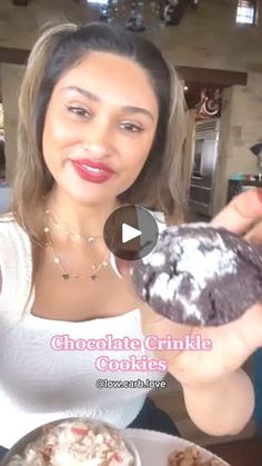 a woman holding a chocolate crinkle cookie in front of a plate of cupcakes