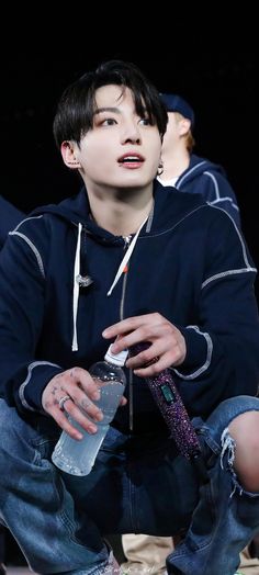 a young man sitting down holding a water bottle and looking up at something in his hand