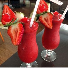 two glasses filled with strawberries and juice on top of a table