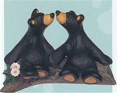 two black bears sitting next to each other on a tree branch with flowers in their paws