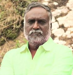 a man in a green shirt standing next to a rock wall and grass covered hillside