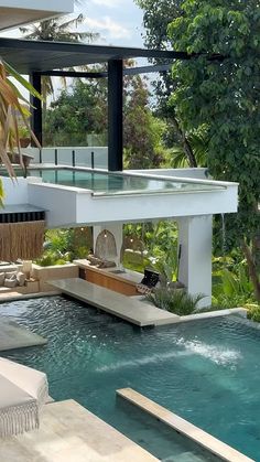 an outdoor swimming pool surrounded by greenery and trees in front of a modern house