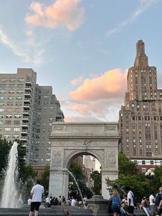 people are walking around in the city with fountains and buildings behind them, as the sun sets